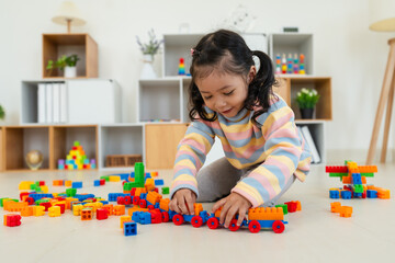 toddler girl playing building blocks or plastic bricks toy at home