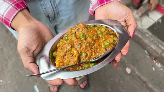 Close-up shot of a person holding a small, oval-shaped metal dish filled with a delicious-looking curry.