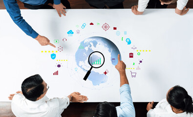 A business team engages in a meeting, analyzing global market trends using digital icons and graphics on a table. The atmosphere fosters collaboration and strategic insight. Trope