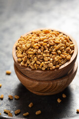 Fenugreek whole seeds in wooden bowl on grey surface with scattered grains around vertical shot. Often used in Indian curries. Concept of organic spice and natural ingredients.