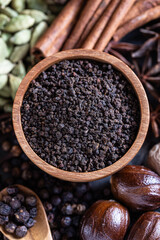 Close-up composition of ingredients for traditional Indian masala chai, featuring whole aromatic spices such as cardamom, cinnamon, cloves, black pepper on black rustic background.