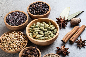Ingredients for preparing garam masala whole aromatic spices in wooden bowls on grey background, close-up view, showcasing traditional Indian cooking and rich natural textures.
