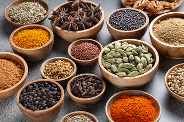 Variety of colorful and vibrant whole and ground Indian spices in wooden bowls on gray background, rich aromatic ingredients for traditional cooking, close-up composition with warm earthy tones.