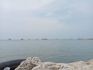 Calm sea view with rocks and ships on the horizon under cloudy sky