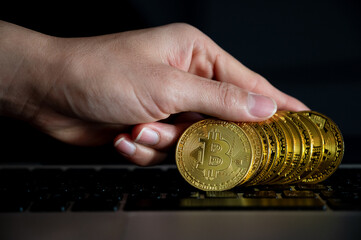 Close up of human hand holding some pieces of golden Bitcoin token on laptop. Bitcoin is one of the popular cryptocurrency, a virtual currency or a digital currency.