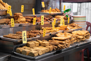Vegetarian Chinese street food display of fried snacks and tofu at a market stall. English translation for Chinese words are vegetarian braised pork, spring rolls, tofu, and etc.