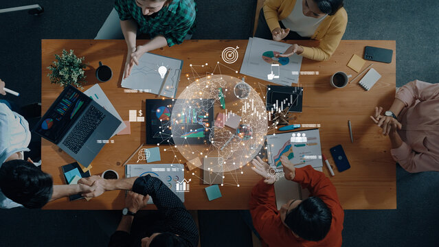 A vibrant team collaborates around a table filled with laptops, notebooks, and data charts, fostering innovation and strategic discussions in a modern office setting. Trope - Powered by Adobe