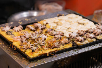 Street food griddle with octopus balls on a large grill at night market.