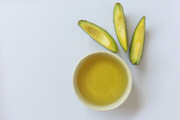 Bowl of avocado oil and fresh avocado slices on white background