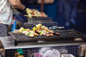 Close-up of grilled meat and vegetable skewers on a street food stall at night market. Ideal for Asian street food visuals, local cuisine, BBQ marketing, night market culture