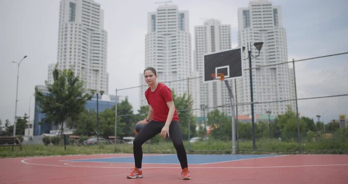 Female basketball player attempts to shoot on an urban outdoor court with high-rise buildings in the background, showcasing determination and athletic skill.