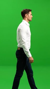 Man walks sideways in a white shirt, blue jeans, over green screen
