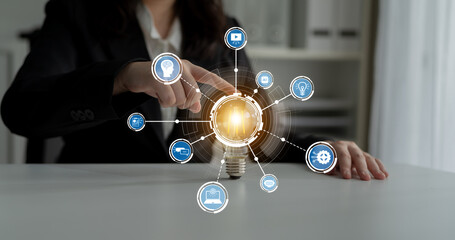 A business professional interacts with a digital light bulb graphic, representing innovation and...