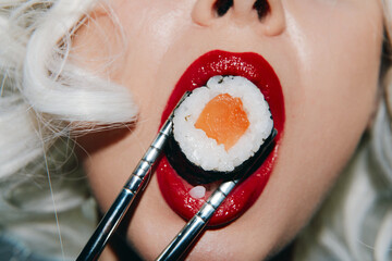 Close-up portrait of a woman with stylish white hair holding sushi with chopsticks, wearing bold...
