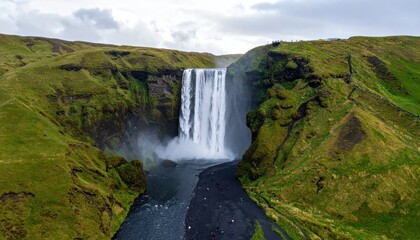 Obraz premium Aerial view of a majestic waterfall cascading down a lush green hillside