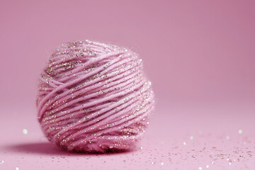 Ball of pink glitter wool yarn on plain studio background with text space
