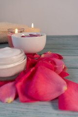 A table with a white bowl of rose petals and two candles. The candles are lit, creating a warm and cozy atmosphere. The table is covered with rose petals, adding a touch of elegance
