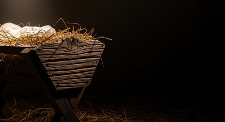 Close-up of a rustic wooden manger with hay and cloth in a dark, dramatically lit setting