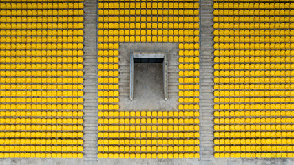 Symmetrical yellow stadium seats from above, a serene geometric pattern of empty spaces	
