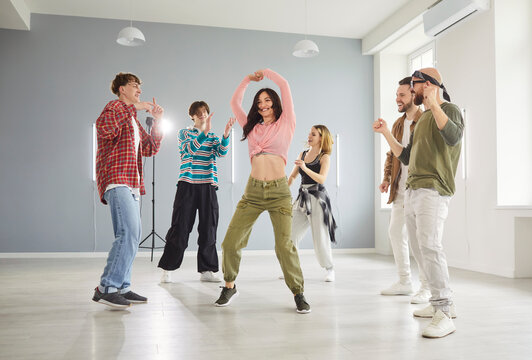Active young people having dancing class lesson, moving energetically to music in dance hall. Cheerful woman demonstrating her dancing talents in circle of friends, having fun together