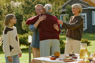 Middle aged Caucasian man smiling while hugging senior Caucasian woman outdoors, young girl and...