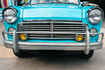 Front view of a vintage turquoise car with chrome grille and headlights, showcasing retro automotive design and classic details Close-up of the front of a classic turquoise car with chrome bumper 