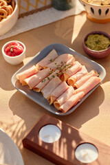 Plate of rolled ham slices garnished with fresh herbs arranged on table surrounded by small bowls...