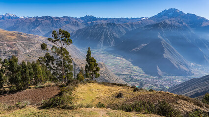 A mountain range with snow-capped peaks against a clear blue sky. In the foreground is a clearing...