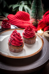 Delicious chocolate cupcakes topped with red buttercream, served on a ceramic plate with a warm festive atmosphere. Perfect sweet dessert for Christmas and New Year celebration.
