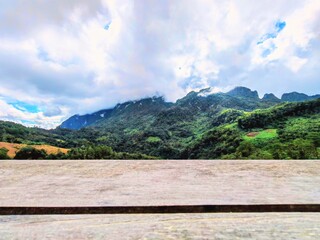 Fototapeta premium Empty Wooden Table or Countertop with Blurred Lush Green Tropical Mountain Landscape and Sky Background for Product Display at Chiang Dao, Thailand.