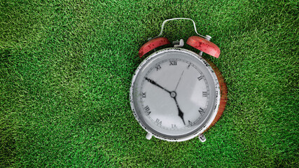 Vintage red alarm clock on green grass background retro scene
