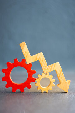 Downward arrow with red and yellow gear wheels representing economic slowdown, industrial recession, production crisis, financial decline, and operational efficiency problems in business systems.