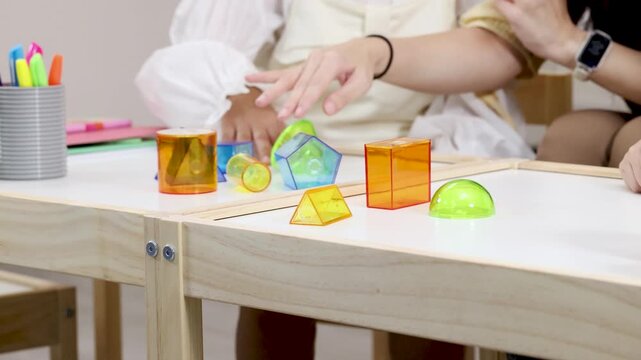 Hands Arranging Colorful Geometric Shapes on Classroom Table
