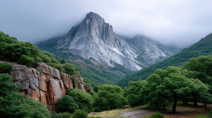 Rugged Granite Mountain Peaks Rise Above Lush Green Trees Under Dramatic Cloudy Skies