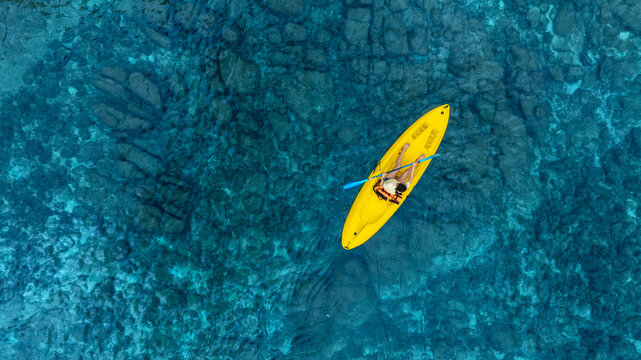 Aerial view woman bright yellow kayak with in the vast expanse of crystal clear turquoise water. The seabeds rocky texture is visible beneath the surface, concept marine environment