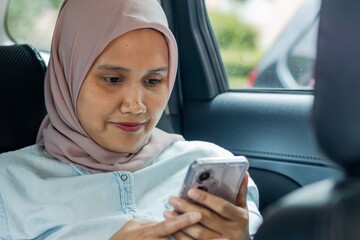 A young Asian Muslim woman in a car using her smartphone while traveling