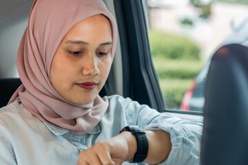 A young Asian Muslim woman looking at her watch while traveling by car