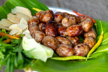 Grilled Thai Isan sausage served with fresh herbs and colorful vegetables on a plate wrapped in banana leaves.