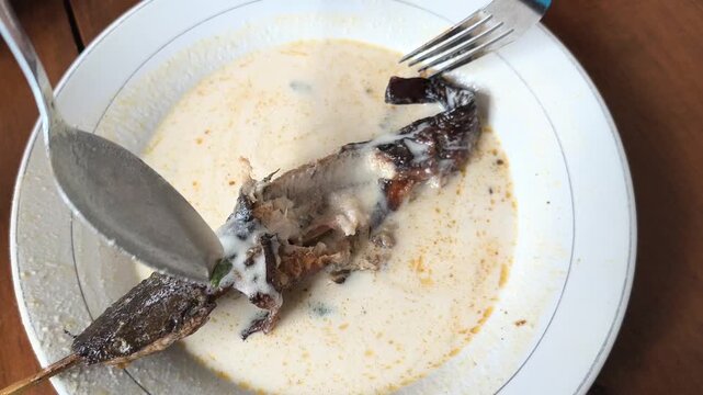 Eat mangut lele with a spoon and fork. Indonesian-style fish curry. A traditional Indonesian dish made with smoked or fried catfish in a spicy coconut milk and some spices. Indonesian food.