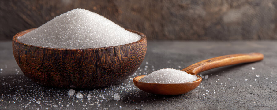 Granulated white sugar in wooden bowl and spoon, rustic kitchen scene with natural texture and warm lighting