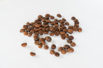 A small, irregular pile of roasted coffee beans scattered on a clean white background, providing a simple yet appealing image for coffee-related themes.