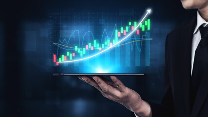 Businessman in suit holds a digital tablet displaying a colorful financial chart with an upward trend, representing growth and analytics in finance. Impute