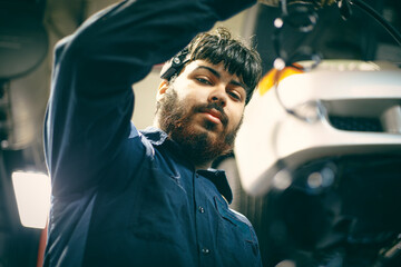 A mechanic in a blue uniform works intently on a piece of machinery. The setting appears industrial, with a mix of shadows and warm lighting.