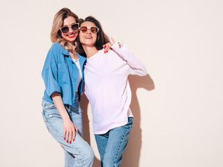 Two young beautiful smiling female in trendy summer clothes. Carefree women posing in studio....