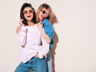 Two young beautiful smiling female in trendy summer clothes. Carefree women posing in studio....