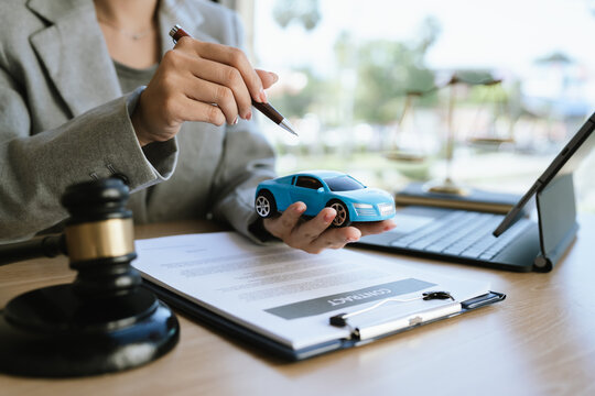 A lawyer signing a car contract with a gavel and a toy car on the desk, symbolizing car law, insurance, or legal agreement.