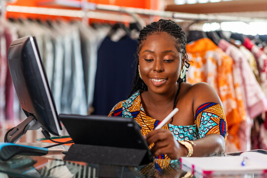African woman, successful small business boutique owner, fashion entrepreneur checking inventory and managing online orders in her clothing store with her smart tablet, SME