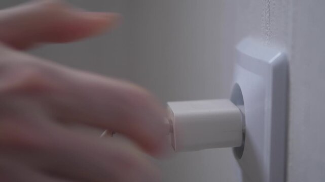 Closeup of mobile phone charger with damaged wire being plugged into outlet, faulty electrical appliance, potential fire hazard