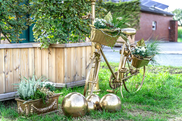 Ein zauberhaftes, ganz in Gold getauchtes Fahrrad steht als strahlendes Symbol der ewigen Liebe auf sattgrünem Rasen. Jeder Korb ist ein kleines Nest aus frischem Grün, zarten weißen Blüten und liebev