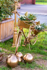 Ein zauberhaftes, ganz in Gold getauchtes Fahrrad steht als strahlendes Symbol der ewigen Liebe auf sattgrünem Rasen. Jeder Korb ist ein kleines Nest aus frischem Grün, zarten weißen Blüten und liebev